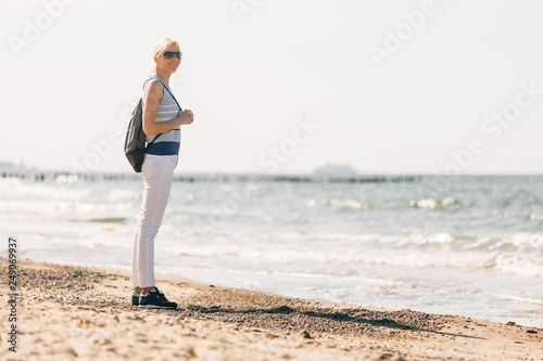 Young, beautiful blonde girl walking at the beach. Stylish woman in white pants and sunglasses near sea