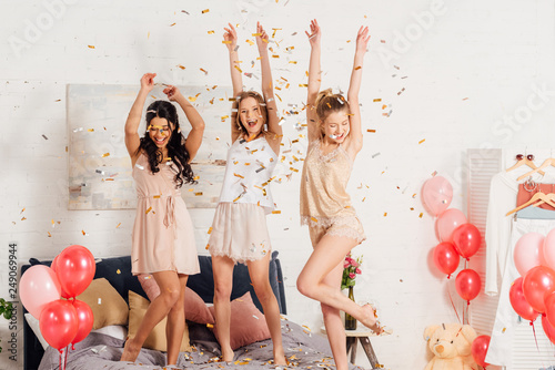 beautiful multicultural girls in nightwear dancing and having fun under falling confetti during pajama party