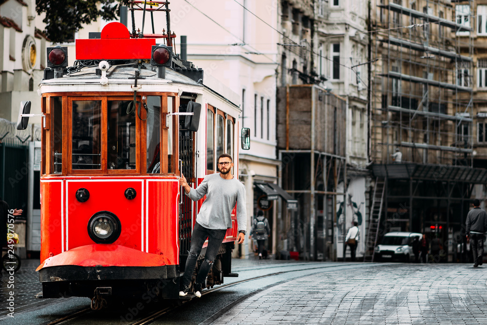Obraz premium Mężczyzna w zabytkowym tramwaju na ulicy Taksim Istiklal w Stambule. Mężczyzna w transporcie publicznym. Stary turecki tramwaj na ulicy Istiklal, Turcja. Portret uśmiechniętego młodego człowieka, pozowanie na ulicy miasta.
