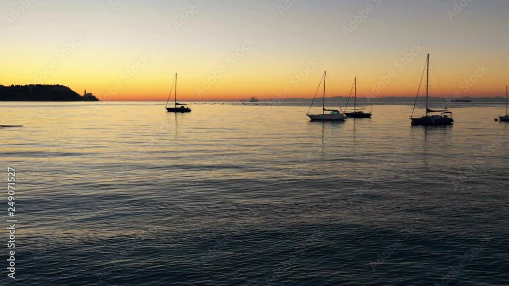 Aerial view with drone flying low over the ocean water between parked sailing boats in a bay with nice sunset vibrant colors in the horizon Aerial view with drone flying low over the ocean water between parked sailing boats in a bay with nice sunset vibrant colors in the horizon