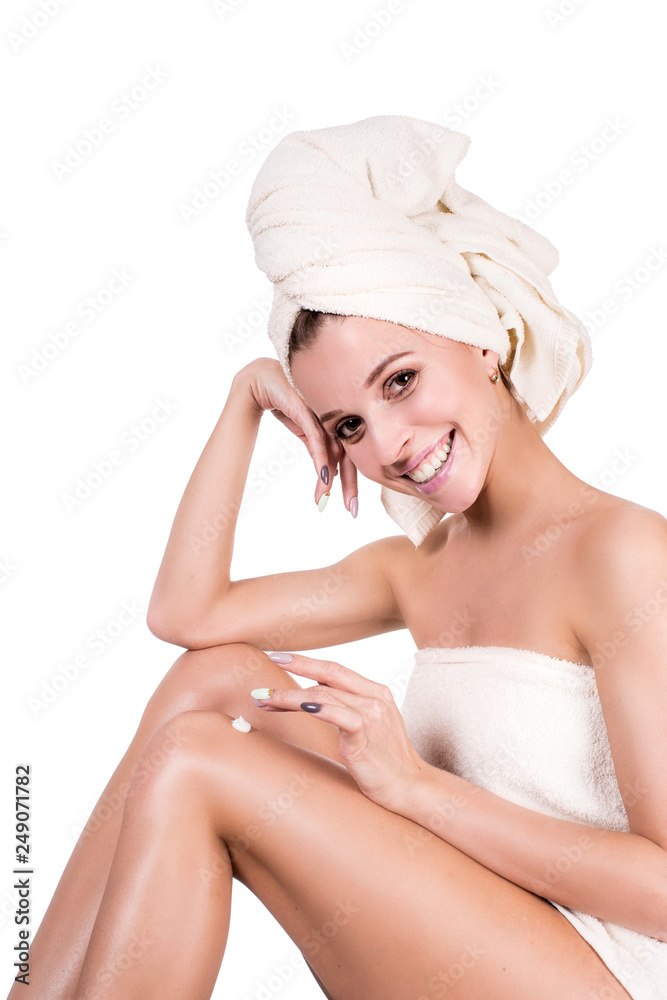 Beautiful young woman in towel sitting on the floor and stroking her legs isolated on white background. Skin care concept. Beautiful young woman in towel sitting on the floor and stroking her legs isolated on white background. Skin care concept.