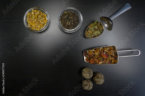 Tea assortment with real tea and tea flowers at black wooden background