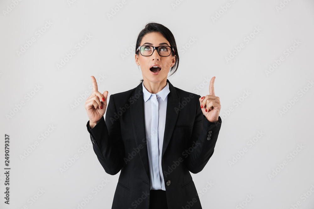 Portrait of cute businesswoman 30s in formal wear and eyeglasses pointing fingers upward, isolated over white background Portrait of cute businesswoman 30s in formal wear and eyeglasses pointing fingers upward, isolated over white background
