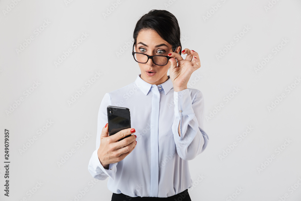 Image of joyous secretary woman wearing eyeglasses using smartphone in the office, isolated over white background