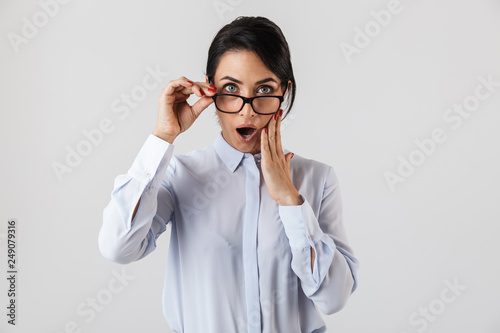 Portrait of excited secretary woman 30s wearing eyeglasses standing in the office, isolated over white background