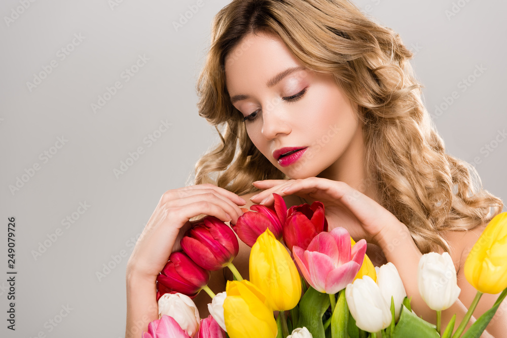 young attractive spring woman touching bouquet of colorful tulips isolated on grey young attractive spring woman touching bouquet of colorful tulips isolated on grey