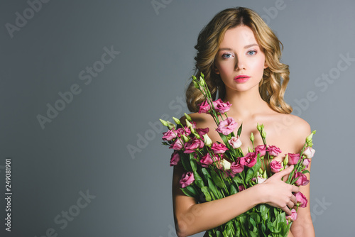 naked woman holding bouquet of eustoma flowers isolated on grey