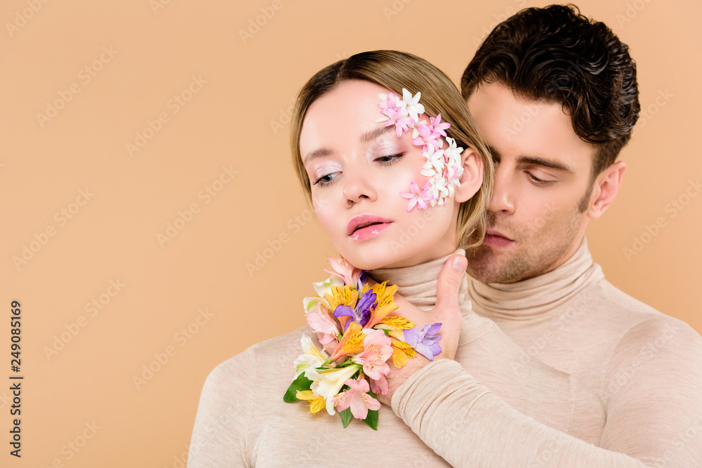 © LIGHTFIELD STUDIOS - tender man with alstroemeria flowers on hand touching face of pretty woman isolated on beige