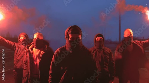 Group of young men in balaclavas with red burning signal flare walking on the road under the bridge photo