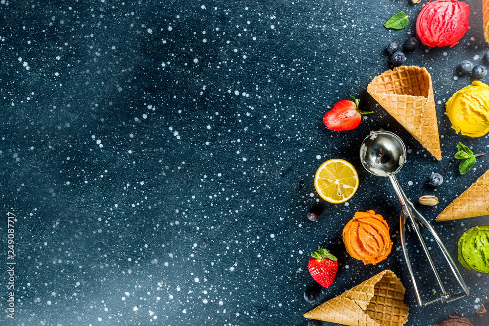 Colorful fruit and berry, nut, chocolate and vanilla ice cream, with waffle ice-cream cones, with fresh fruit and berries, top view copy space dark blue background