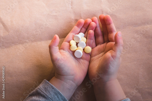 Baby hands with pills on paper background. Sick Child Has Medicine and Vitamins, Closeup, Neutral Background
