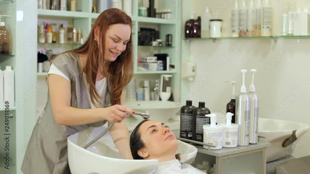 Woman hairdresser pours water on the client's hair, washes them with shampoo before cutting. Woman hairdresser pours water on the client's hair, washes them with shampoo before cutting.