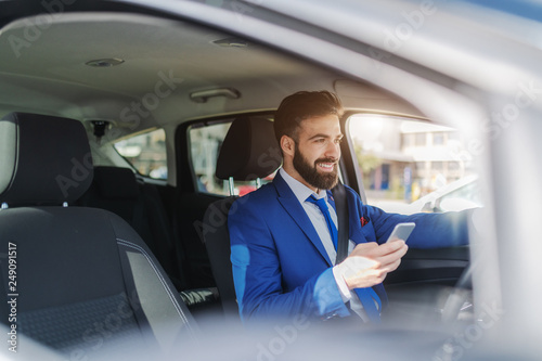 Close up of smiling businessman using smart phone while sitting in his car and leaning on the window. © dusanpetkovic1