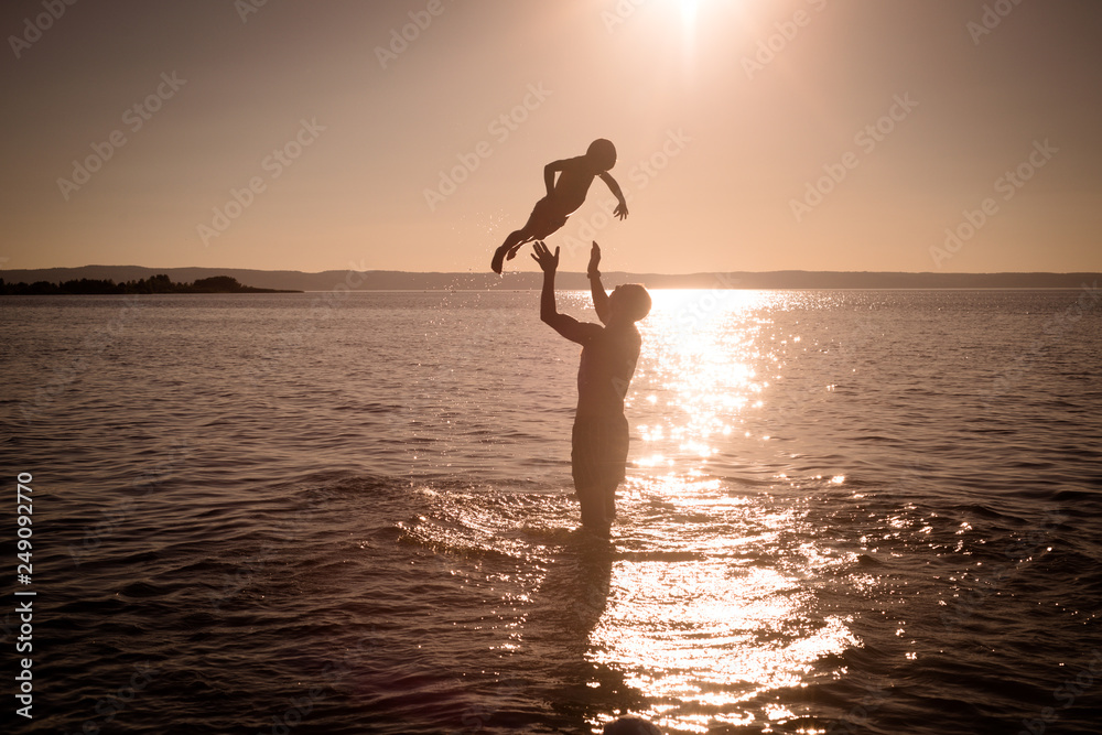 Silhouette of the father throwing his son in the air in water