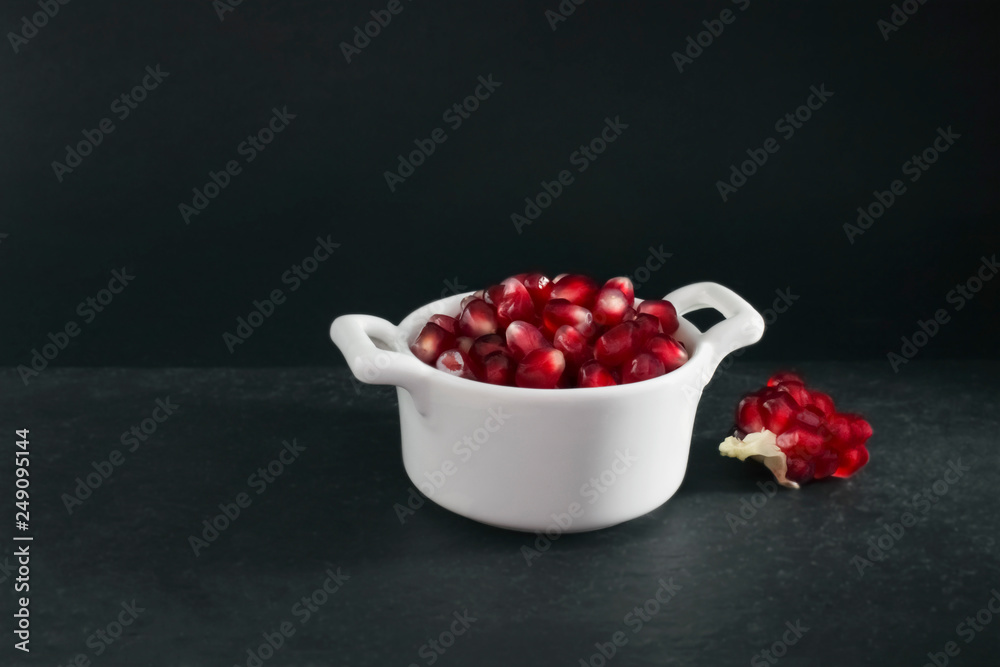 Organic fresh pomegranate seeds in white bowl on the black stone plate. Organic fresh pomegranate seeds in white bowl on the black stone plate.