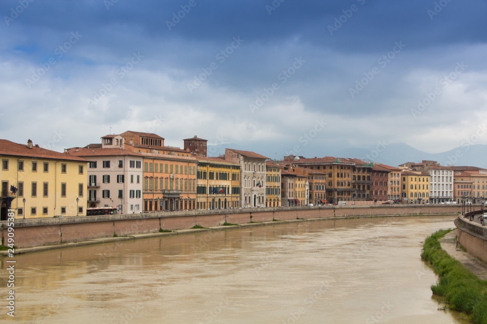 Old colorful buildings along the Arno river. Pisa cityscape. Embankment of the Arno river in Pisa. Gloomy rainy and cloudy day. Pisa, Italy.