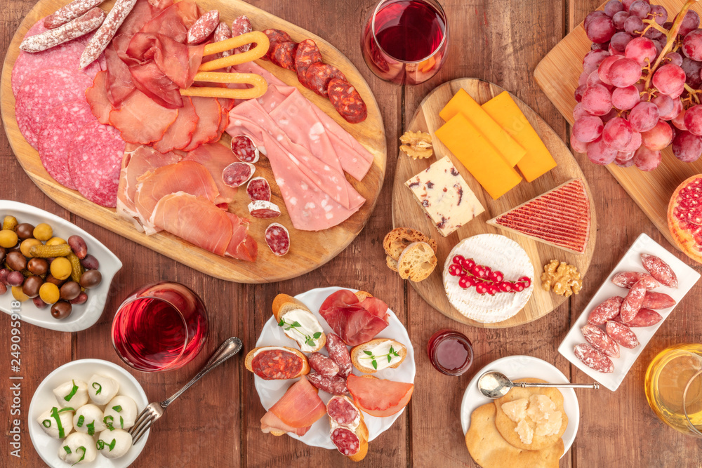 Gourmet Charcuterie. An assortment of sausages and hams, deli meats, and a cheese platter, shot from the top on a dark rustic background with wine and olives