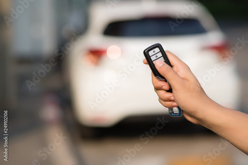 The focus image of the hands of people who are pressing on the remote car key has a blur background image of a car in the morning in Bangkok, Thailand.