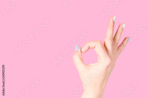 Beautiful fenale hand with trendy colorful blue and white fresh gel manicure. Woman showing okey sign isolated on pink background Horizontal color photography.