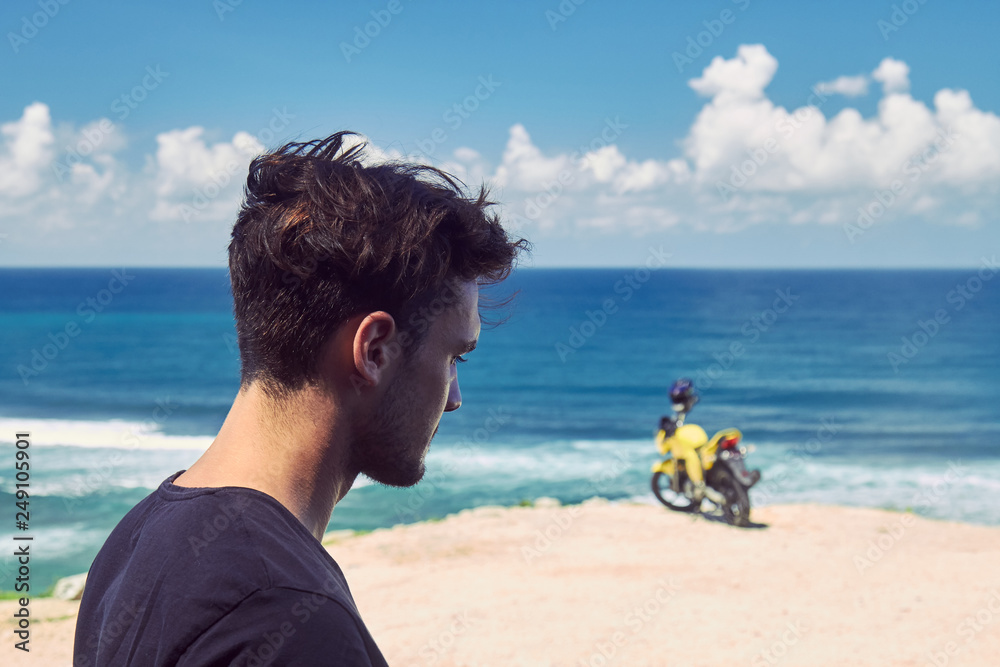 Fototapeta premium Young handsome man standing near motorcycle on the tropical beach.