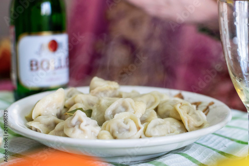 Plate of hot dumplings with steam and glass of champagne at background on the table on holiday