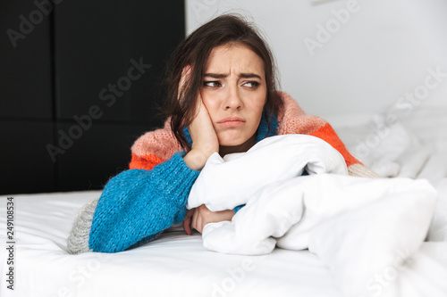 Billede på lærred Photo of upset woman 20s wearing sweater, lying in bed at home