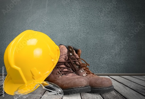 Yellow working hard hat, goggles and work boots on  background