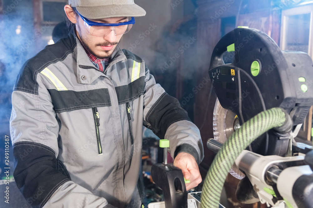 A young male carpenter installs a workpiece in a circular machine. Handwork. Starting a business A young male carpenter installs a workpiece in a circular machine. Handwork. Starting a business