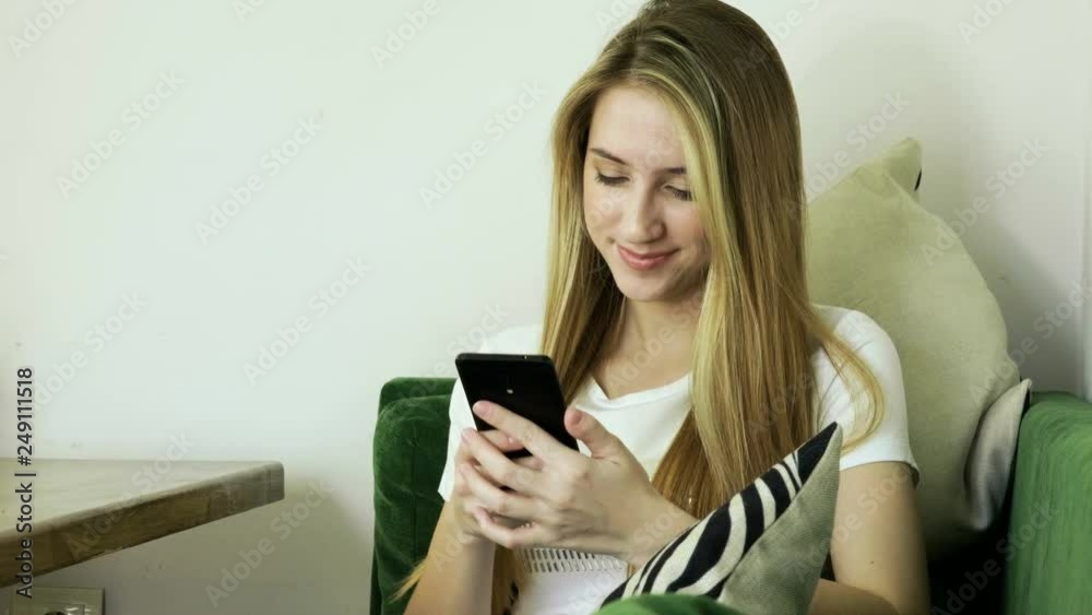 Young smiling woman using smartphone and texting on mobile phone in modern cafe. 4K