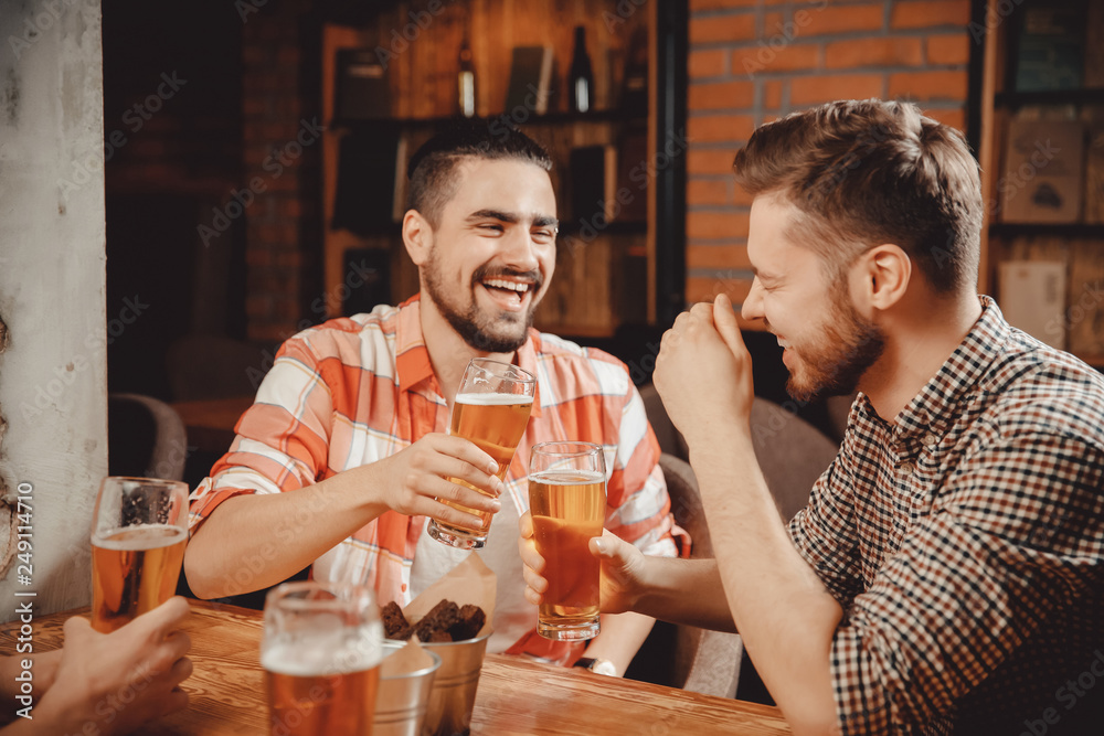 Two men relax bar, laugh drink draught beer in pub, clanging glasses