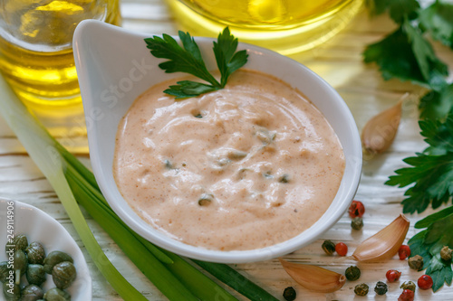 Homemade traditional French remoulade sauce in a White bowl with ingredients-capers, parsley, green onion, mustard, fragrant vinegar, olive oil, garlic on a light wooden table. dip. Selective focus photo