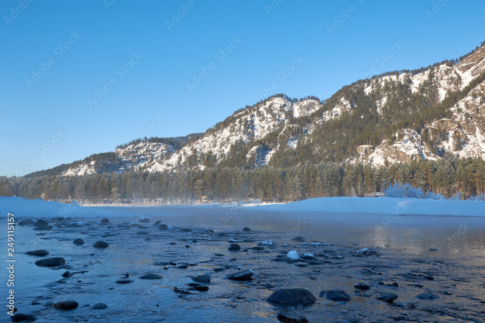 Mountain lake. Blue water and large dark stones surrounded by snow-capped mountains Blue sky. Frosty day.