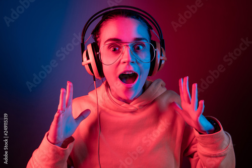 Surprised pretty woman with headphones listening to music over red neon background at studio.