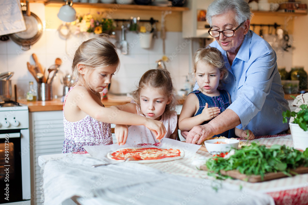 Children chefs are cooking italian pizza in cozy home kitchen for family dinner. Grandmother is teaching cute kids to cook food. Three little girls are helping old senior woman. Lifestyle moments. Children chefs are cooking italian pizza in cozy home kitchen for family dinner. Grandmother is teaching cute kids to cook food. Three little girls are helping old senior woman. Lifestyle moments.