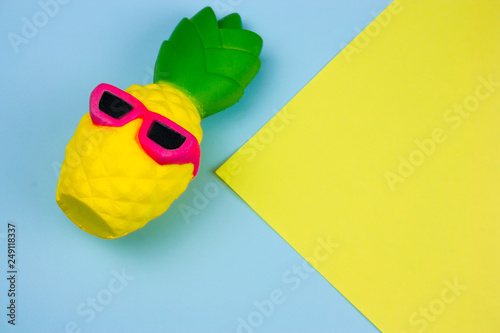 top view summer vibrant blue and yellow background with funny pineapple toy in sunglasses, copy space