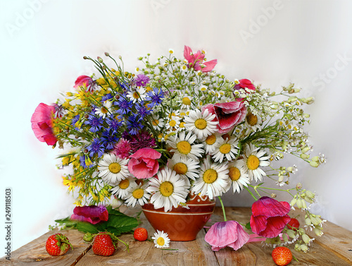 Still life of field daisies and different flowers in a clay vase and a basket with berries on the table