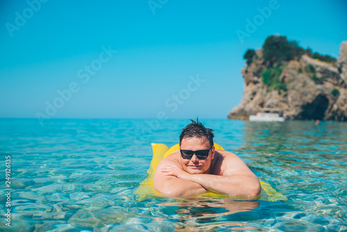 young man at yellow inflatable mattress in clear transparent water