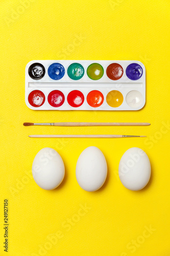 Happy Easter concept. Preparation for holiday. Decorative eggs colorful paints and brushes isolated on trendy yellow background. Simple minimalism flat lay top view copy space