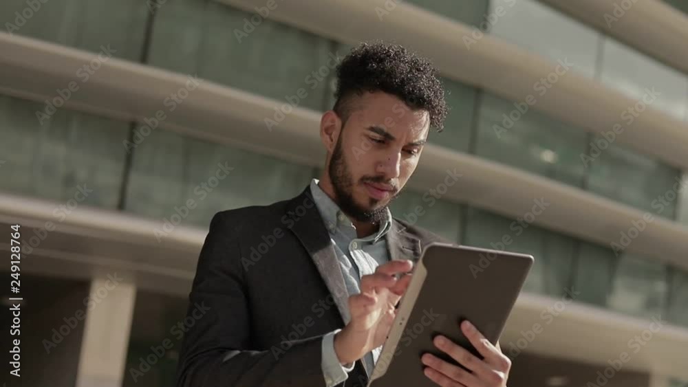 Focused middle eastern young man using tablet outdoor. Focused middle eastern young man using tablet outdoor.