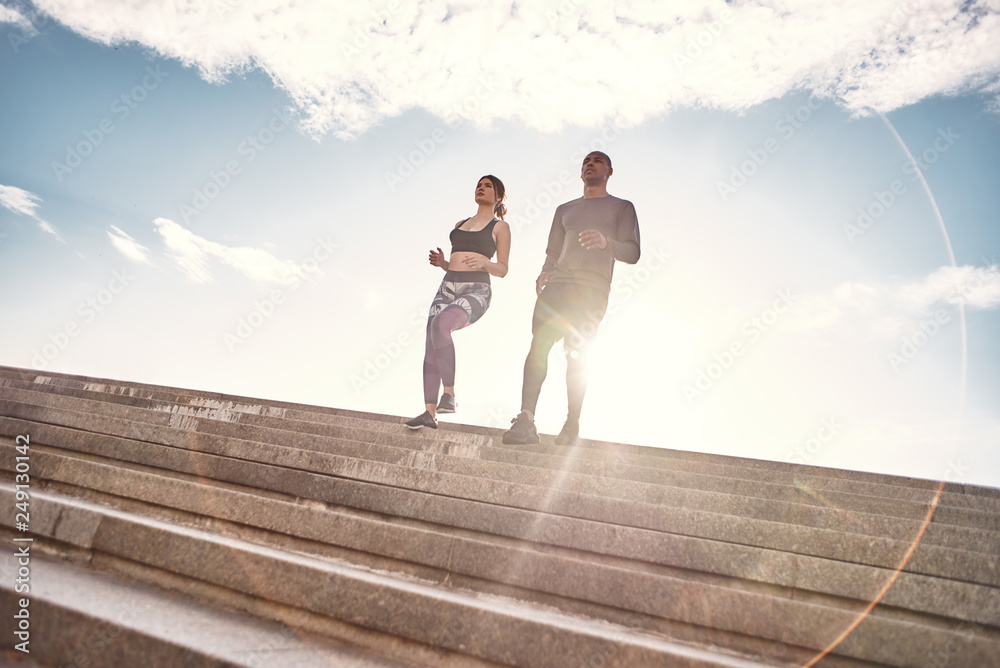 Obraz premium Training together is fun. Full length portrait of cute and young interracial couple in sportswear running down stairs against sunny and clear sky. Common hobbies