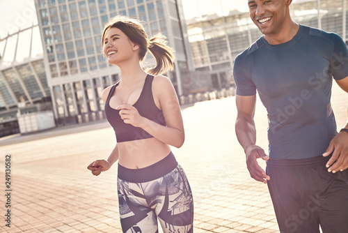 Perfect training. Positive mixed race couple  sporty african man and brunette girl in sportswear running together on a sunny warm day.