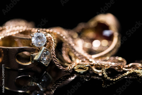 Real gold rings with diamonds, gold chains close up shot on shiny black background.