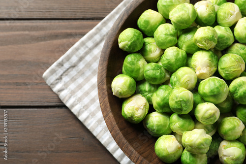 Bowl of fresh Brussels sprouts and napkin on wooden background, top view with space for text