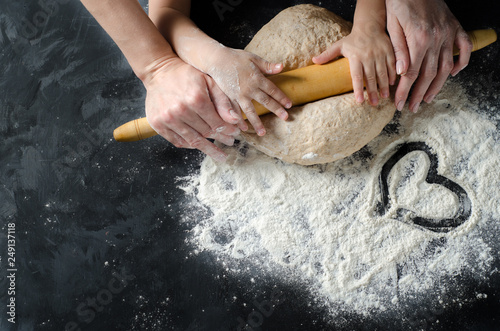 Mother and children hands rolled dough with a rolling pin on the black table. Top view.