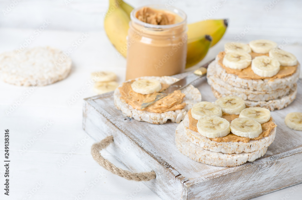 Healthy breakfast with rice cakes with peanut butter and slices of banana on white wooden table Healthy breakfast with rice cakes with peanut butter and slices of banana on white wooden table