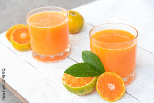 two glasses of orange juice and fresh oranges on white wooden base