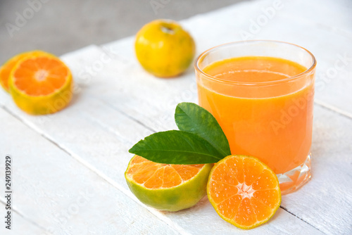 a glass of orange juice and fresh oranges on white wooden base