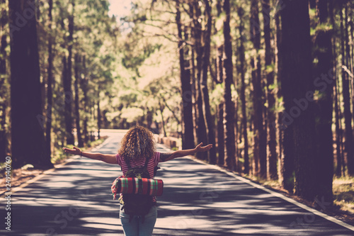 Eternity and success satisfaction life concept with lonely girl curly hai rin the middle of long road in the forest with open arms and backpack - wanderlust and travel style people photo
