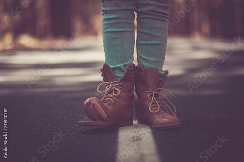 Travel wanderlust lifestyle concept with pair of broken trekking shoes closeup in the middle of an asphalt long road - defocused background - vintage filter and dark tones photo