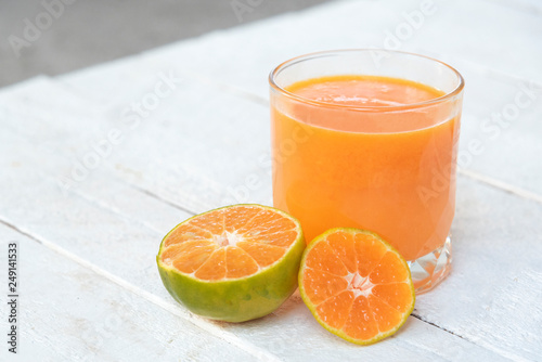 a glass of orange juice and fresh oranges on white wooden base